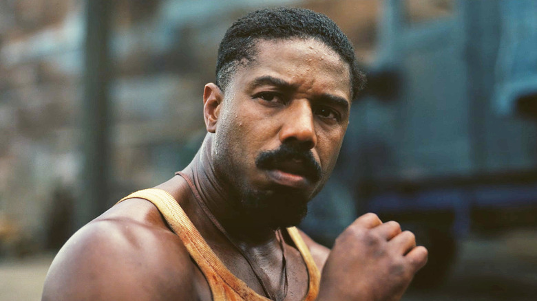 Michael B Jordan as Elijah 'Smoke' Moore, sitting on the ground outside the sawmill, in Sinners