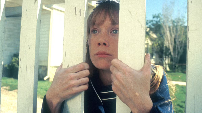 Sissy Spacek as Carrie White looking sad as she peers through a white picket fence in Carrie (1976)