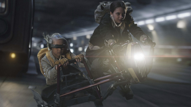 Ryan Kiera Armstrong como Fern andando de bicicleta espacial por um túnel, enquanto Kyriana Kratter como KB anda de sidecar em Skeleton Crew