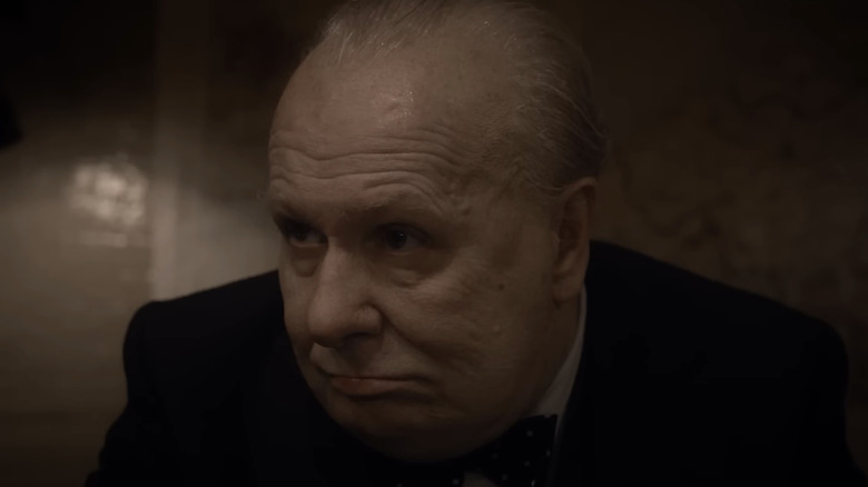 Gary Oldman's Winston Churchill is seen in closeup in a dark room in Darkest Hour