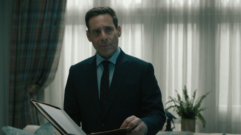 Claude Whelan dari James Callis berdiri memegang file di ruang tamu di Slow Horses