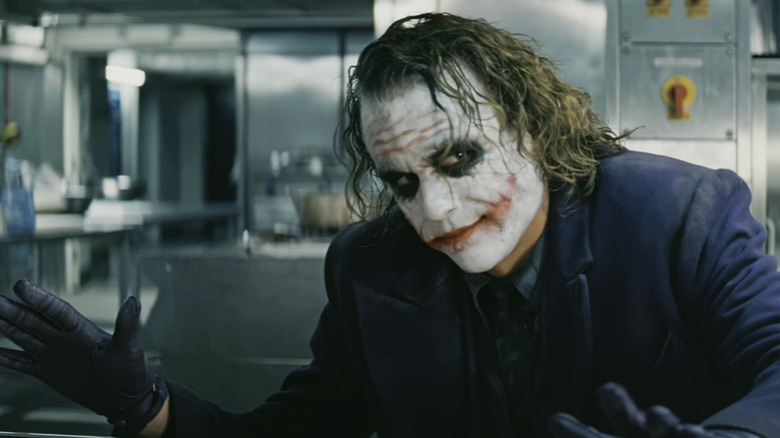 Heath Ledger's Joker holds out his hands in a kitchen in The Dark Knight Rises