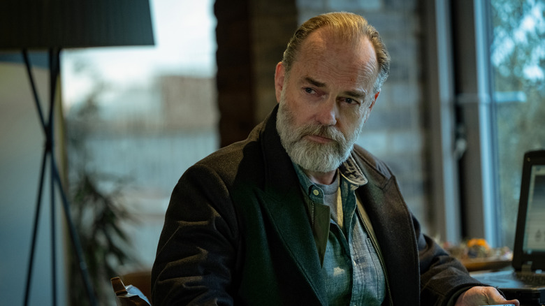 Hugo Weaving's Frank Harkness sits holding a phone in Slow Horses