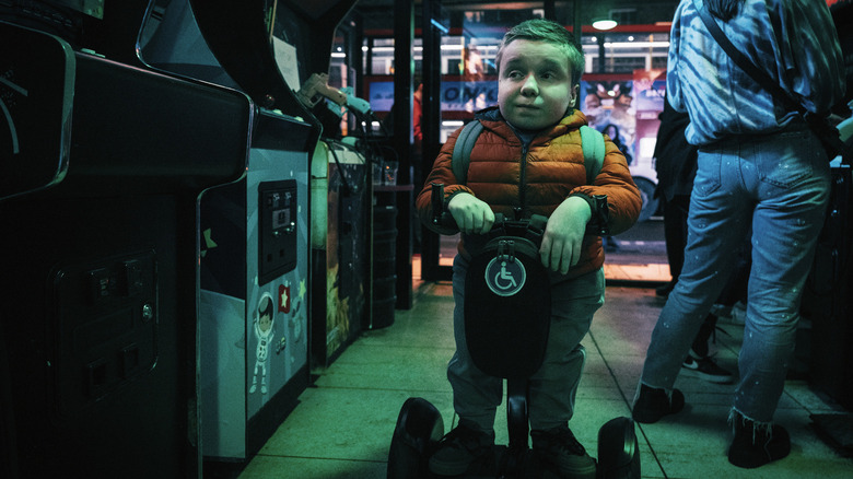 Reece Nesmith riding a motorized vehicle through an arcade in Slow Horses Season 6