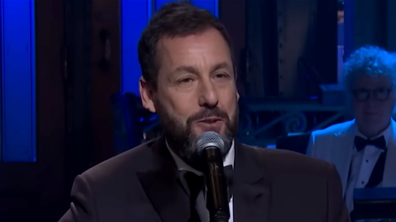 Adam Sandler singing and playing guitar in front of a video of Gilda Radner during SNL 50