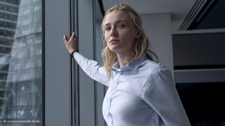 Zara en chemise bleue avec sa main sur une fenêtre dans Steal