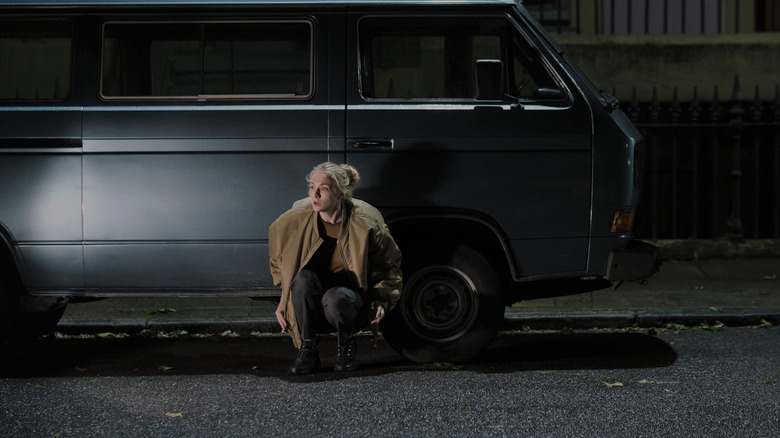 Zara accroupie près d’une voiture dehors dans Steal