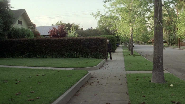 Michael Myers stands behind a hedgerow in Halloween