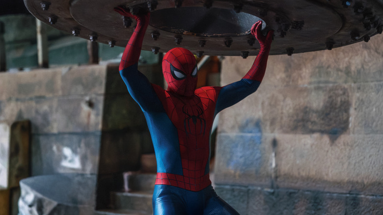 Tom Holland as Peter Parker wearing his superhero outfit and lifting a heavy cylindrical object in Spider-Man: Brand New Day