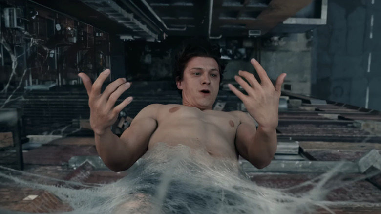 టామ్ హాలండ్ యొక్క పీటర్ పార్కర్ స్పైడర్ మాన్: బ్రాండ్ న్యూ డేలో వెబ్ కోకన్ నుండి తలక్రిందులుగా వేలాడుతున్నప్పుడు అతని చేతులను చూస్తున్నాడు