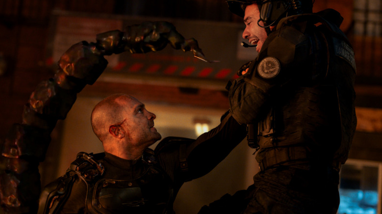 Michael Mando as Mac Gargan wearing an armored suit holding up a soldier in a threatening pose in Spider-Man: Brand New Day