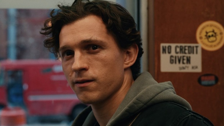 Tom Holland as Peter Parker sitting at a café and looking off-screen wistfully in Spider-Man: Brand New Day