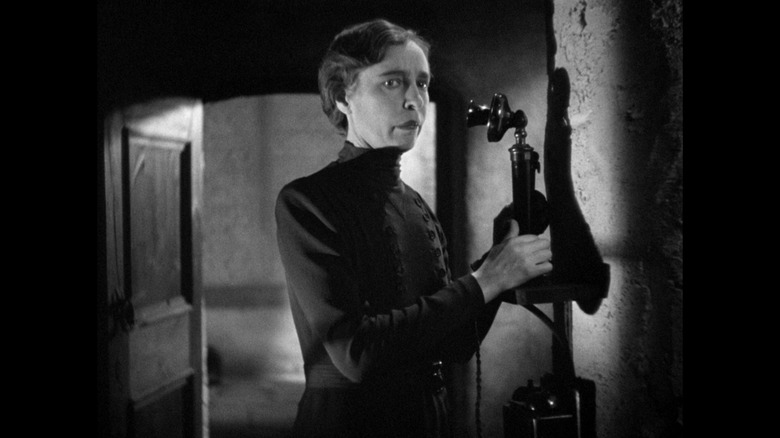 A woman looking concerned next to an old-fashioned phone in The Man Who Knew Too Much