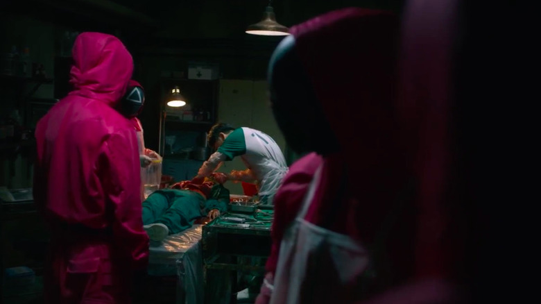 Player 111 harvesting organs from a dead player while pink guards look in in Squid Game season 1