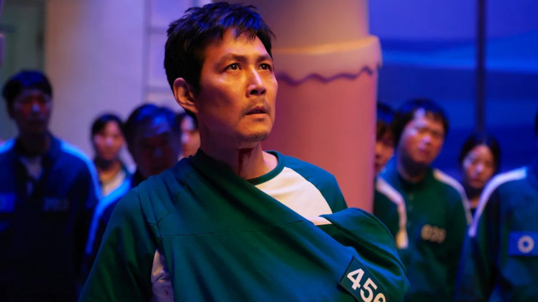 Squid Game, Gi-hun holding the baby Player 222 in his arms, surrounded by other players