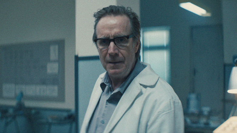 Rhys Ifans as the Chief Designer wearing a lab coat in Star City