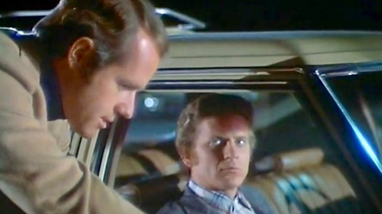 A man in a car looking at Questor outside of the car in The Questor Tapes