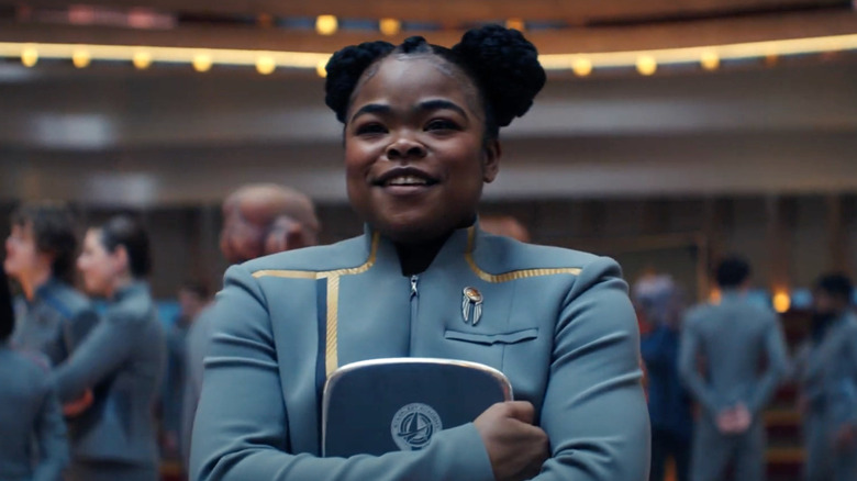 SAM smiles as she grips her tablet while standing amongst a group of cadets in her grey cadet uniform in "Star Trek: Starfleet Academy"