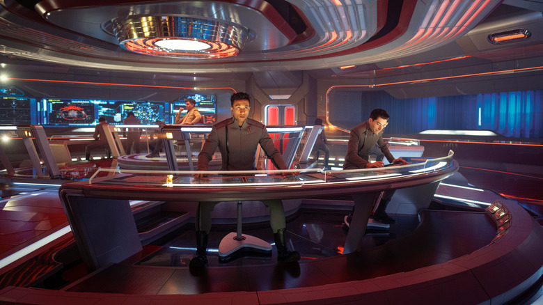 Tig Notaro as Reno sitting at the captain's chair while Sandro Rosta as Caleb and Romeo Carere as Ocam man their stations on the bridge in Star Trek: Starfleet Academy