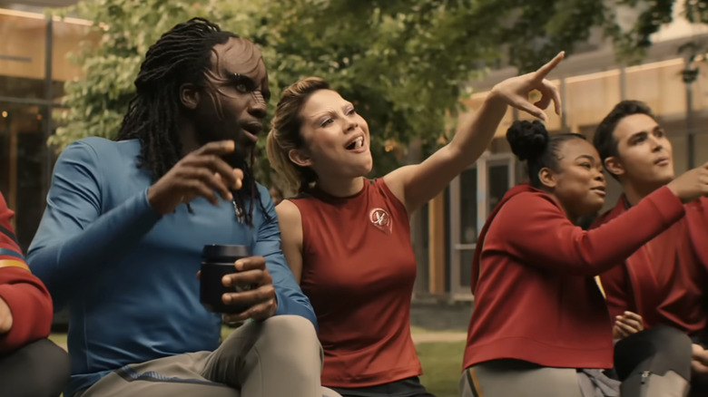 A Klingon wearing a blue shirt sits next to a bunch of red-shirt-wearing humans in Starfleet Academy