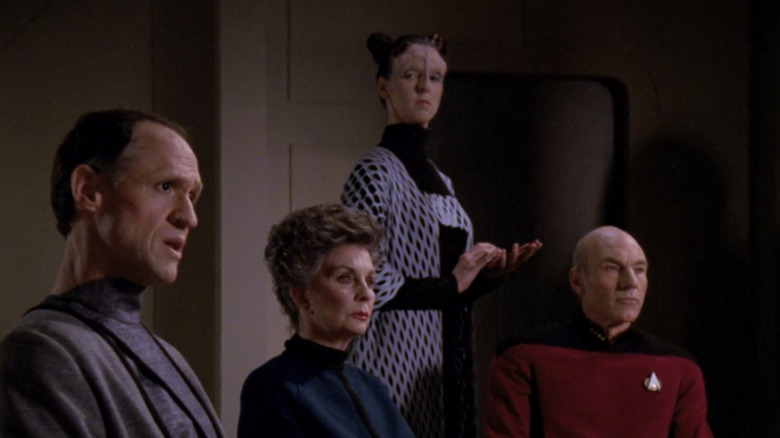 Sabin Genestra, Norah Satie, Nellen Tore en Captain Picard zitten aan een tafel in Star Trek: The Next Generation