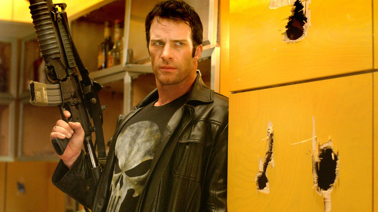 தாமஸ் ஜேன் ஃபிராங்க் கோட்டையாக துப்பாக்கியை பிடித்துக்கொண்டு தி பனிஷரில் தோட்டா துளைகளுடன் சுவரில் நிற்கிறார்