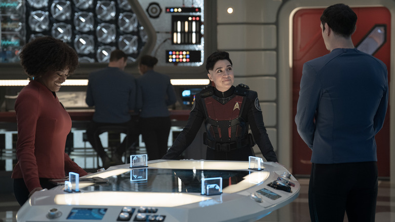 Celia Rose Gooding como Uhura, Melissa Navia como Ortegas e Ethan Peck como Spock na terceira temporada, episódio 9 do Strange New Worlds, com Ortegas Standing Center e Uhura rindo