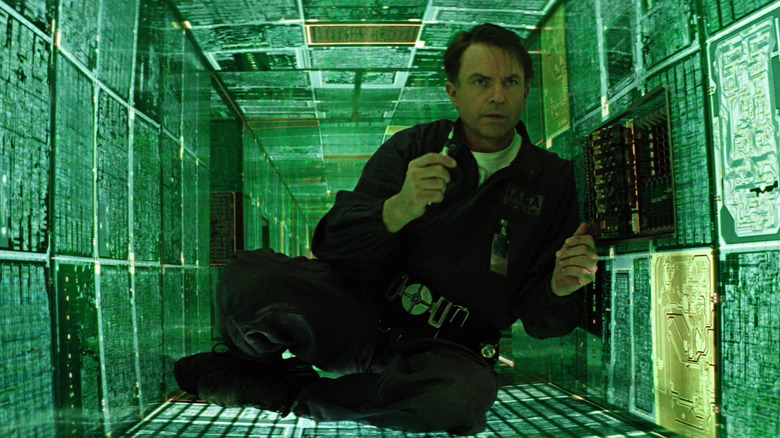 Sam Neill como Dr. Weir, cercado por painéis verdes brilhantes no evento de evento