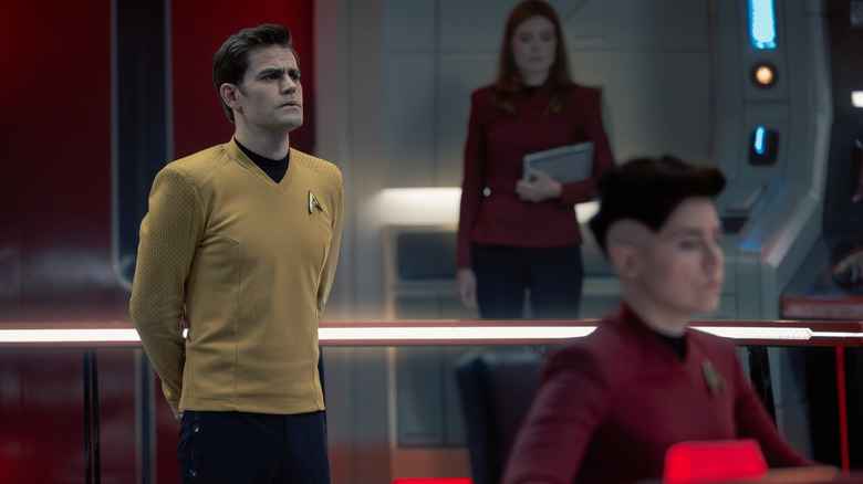 Paul Wesley as James T. Kirk standing at attention on a starship bridge alongside Ewa Wolniczek as Yeoman Vanek and Melissa Navia as Erica Ortegas in Star Trek: Strange New Worlds