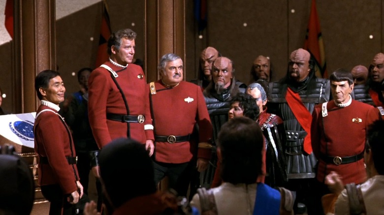Kirk, Scotty, and others standing around in a large political chamber in Star Trek VI: The Undiscovered Country