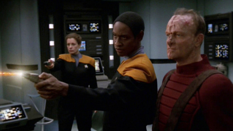 Tuvok firing a phaser while a Starfleet crewperson and an alien look on in Star Trek: Voyager