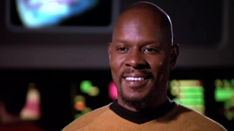 Benjamin Sisko (Avery Brooks) stands smiling in a classic Star Trek uniform in Star Trek: Deep Space Nine