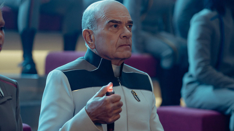 Robert Picardo as the Doctor holding up a handheld device in an auditorium surrounded by students in Star Trek: Starfleet Academy