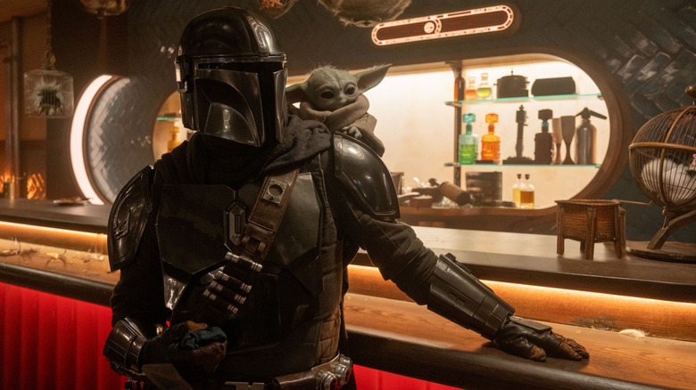 Pedro Pascal as Din Djarin leaning against a counter at a diner with Grogu on his shoulder in The Mandalorian and Grogu