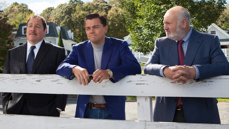 Jon Favreau as Manny Riskin standing in front of a white fence next to Leonardo DiCaprio as Jordan Belfort and Rob Reiner as Max Belfort in The Wolf of Wall Street