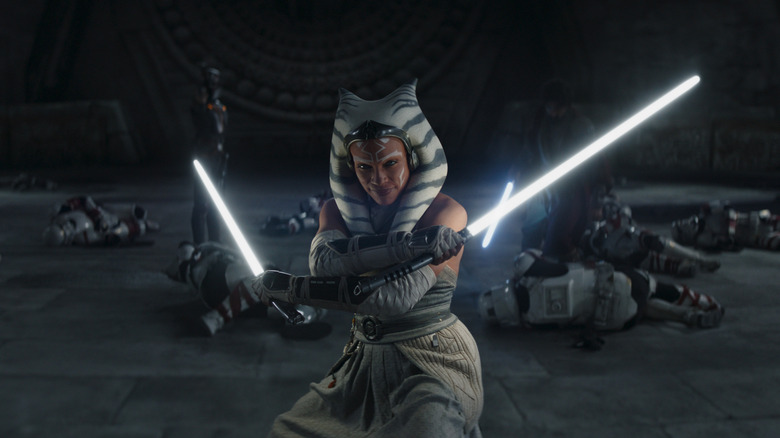 Natasha Liu Bordizzo as Sabine Wren and Eman Esfandi as Ezra Bridger standing behind Rosario Dawson as Ahsoka Tano wielding dual lightsabers in Ahsoka