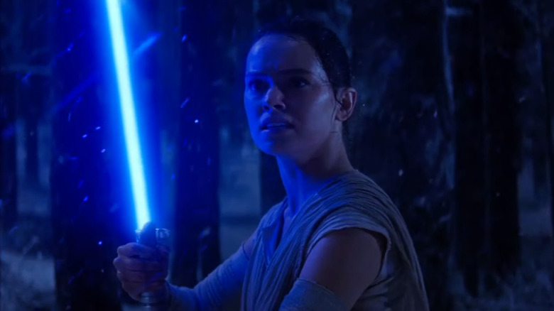 Rey holds a lightsaber in The Force Awakens