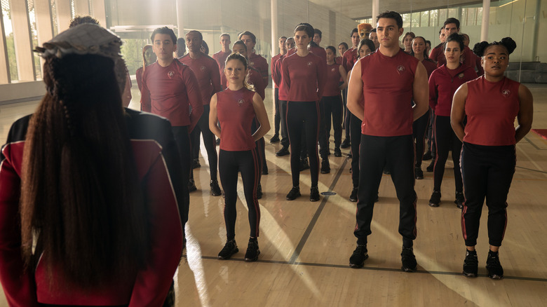 Gina Yashere as Lura standing across from Romeo Carere as Ocam Sadal, Bella Shepard as Genesis Lythe, George Hawkins as Darem Reymi, and Kerrice Brooks as Sam standing at attention in a gym in Star Trek: Starfleet Academy