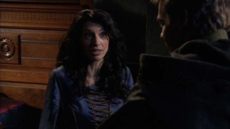 Vala Mal Doran by Claudia Black talks to someone off screen while wearing a blue dress in Stargate SG-1