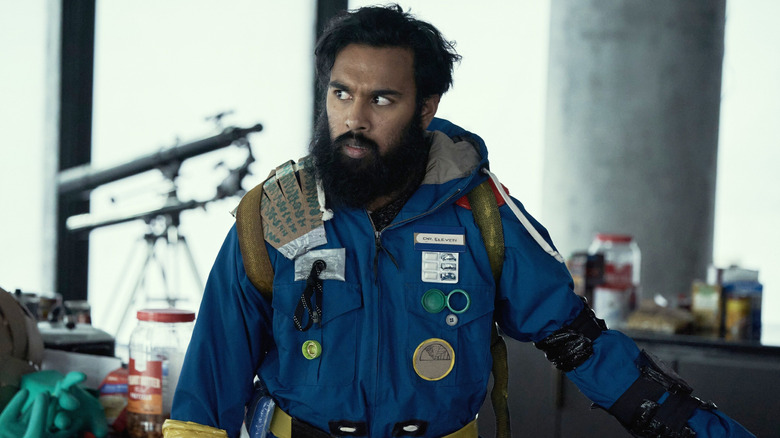 Himesh Patel as Jeevan Chaudhary wearing a blue jacket covered in various items in Station Eleven