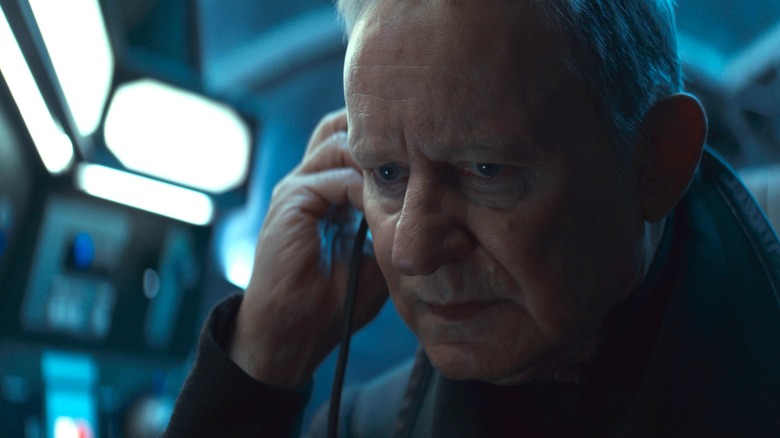 Stellan Skarsgård as Luthen Rael holding an earpiece and looking concerned in Andor season 2