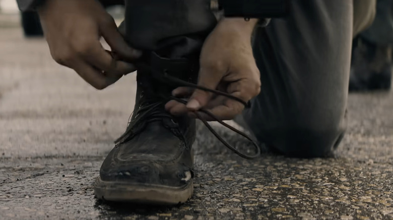 A character tying their shoe in The Long Walk