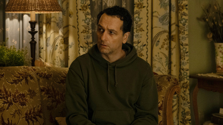 Matthew Rhys as Mayor Tom Loftis sitting on a couch looking worried in Widow's Bay