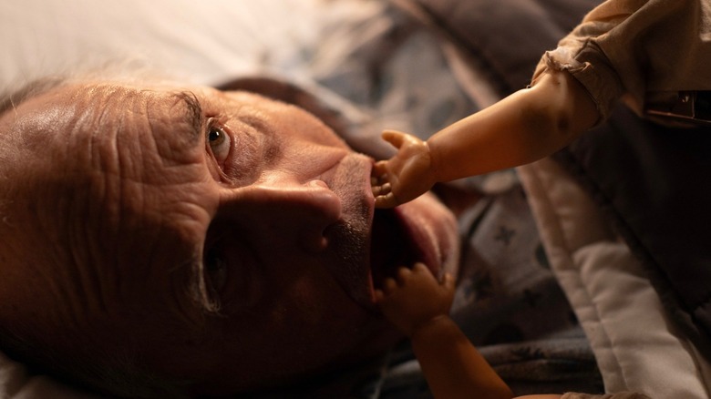 A man with doll arms in his mouth in The Rule of Jenny Pen
