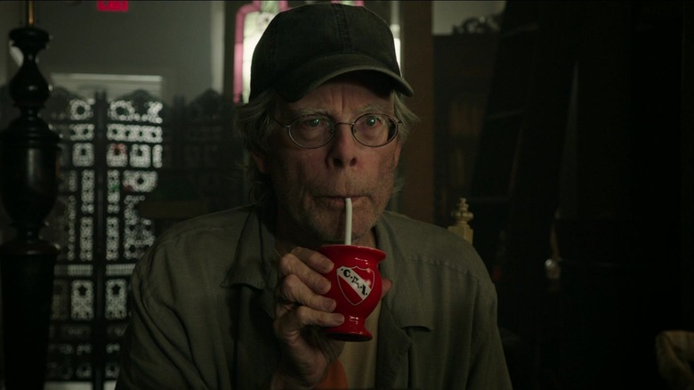 Stephen King's shopkeeer sips from a tiny red cup in It Chapter Two