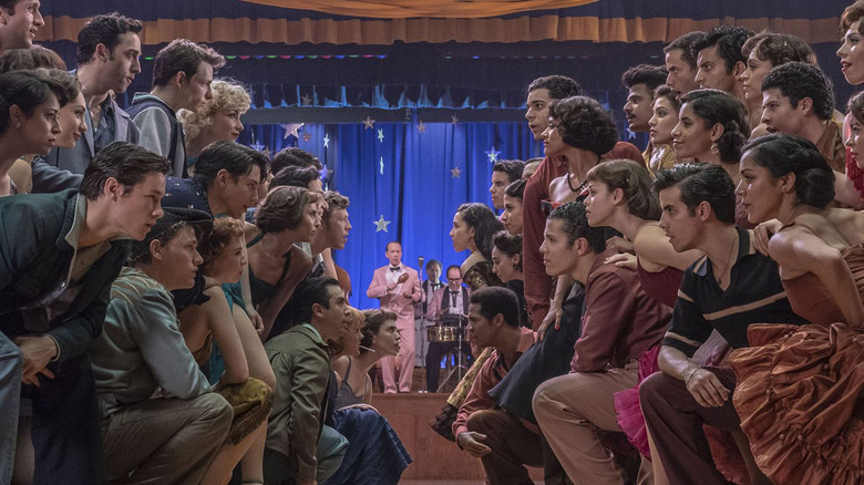 two groups of people kneeling in front of each other in an auditorium with a band behind them on a stage