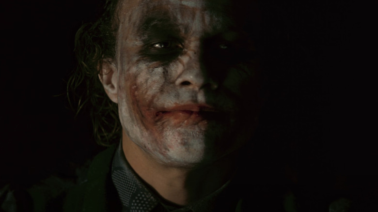 Heath Ledger as the Joker sits in the dark in The Dark Knight