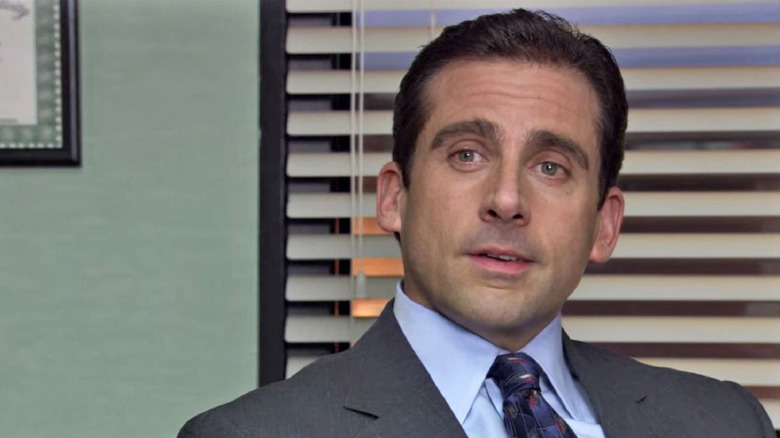Michael Scott sits at his desk and looks at the off-screen cameraperson on The Office