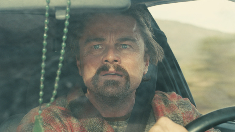 Leonardo DiCaprio as Bob looking in the rearview mirror of his car in One Battle After Another