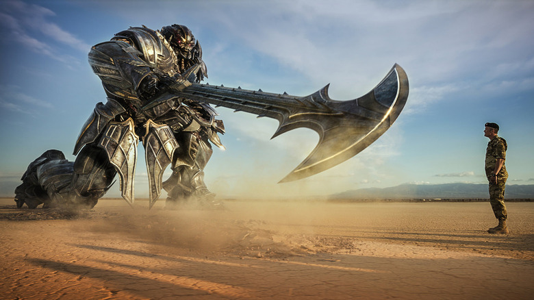a transformer with a round blade for an arm pointing it at a man in an empty desert